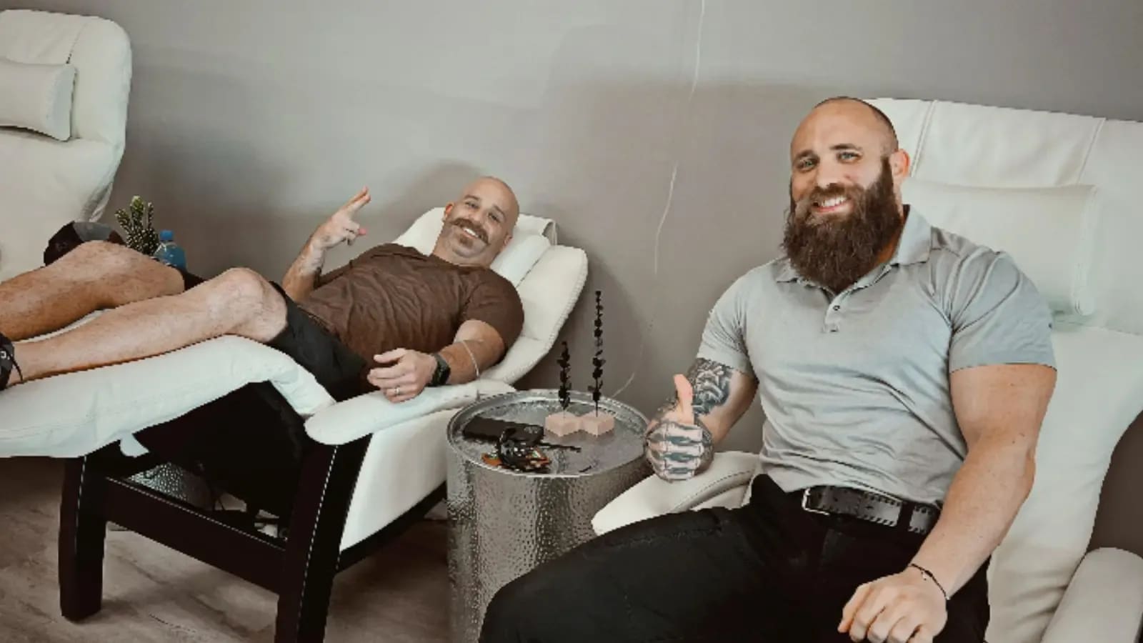 Two men smiling in white recliners at Alpha IV Therapy, one giving a thumbs-up