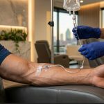 A medical professional with blue gloves on is connecting a medical line into another person's arm